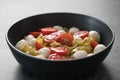 Fettuccine pasta with pesto, mozzarella and cherry tomatoes in black bowl on concrete background