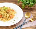 Fettuccine pasta with salmon on a white plate, on a wooden background, next to a basket with greens and cutlery: a spoon and a for Royalty Free Stock Photo