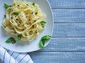 Fettuccine served on white plate with basil and capers on light grey wooden background. Selective focus, copy space