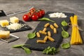 Fettuccine and spaghetti with ingredients for cooking pasta, tomato, arugula on black rock plate. Royalty Free Stock Photo