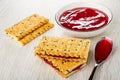 Cookies, bowl with cherry jam, sandwiches from crackers with flax seeds, spoon with jam on wooden table Royalty Free Stock Photo