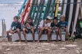 Few cute Indonesian teenagers sit with mobiles at beach on beach sofa with lot surfing boards at background, close up photo. Sup