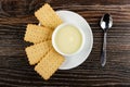 Few cookies and white bowl with condensed milk in saucer, spoon on wooden table. Top view Royalty Free Stock Photo