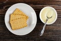 Few cookies in saucer, spoon in white bowl with condensed milk on wooden table. Top view Royalty Free Stock Photo