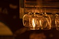 A few glass goblets for wine, martini, alcoholic drinks hang upside down above the bar. Warm evening yellow light in a cafe Royalty Free Stock Photo