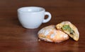 A few homemade, filled cookies lie on a wooden table top with an espresso cup in the background