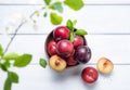 A few juicy and sweet  red plums in bowl  with green leaves  on a white  wood background. Top view and copy space Royalty Free Stock Photo