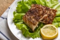 Two pieces of grilled fish fillet with the fresh leafs of lettuce and lemon on old wooden background. Top view. Close up.