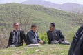 A few rural men sit on the grass. Trees, mountains and forest are visible in background, Iran, Gilan