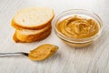 Slice of bread, spoon with peanut butter, transparent bowl with peanut butter on wooden table Royalty Free Stock Photo