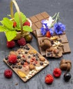A few slices of chocolate, berries, flowers, and a basket of strawberry leaves on a black slate background Royalty Free Stock Photo