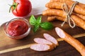 Few slices of thin smoked sausages near ketchup and raw tomato on a brown wooden cutting board. Sausage and fresh vegetables as a Royalty Free Stock Photo
