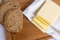 A few slices of yellow butter cut off from a large piece with a knife on a brown wooden cutting board. Several slices of rye bread Royalty Free Stock Photo