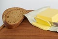 A few slices of yellow butter cut off from a large piece with a knife on a brown wooden cutting board. Several slices of rye bread Royalty Free Stock Photo