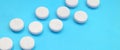A few white tablets lie on a bright blue background surface. Background image on medical and pharmaceutical topics