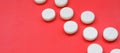 A few white tablets lie on a bright red background surface. Background image on medical and pharmaceutical topics