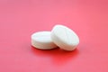A few white tablets lie on a bright red background surface. Background image on medical and pharmaceutical topics