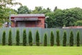 a few young cypresses Cupressus sempervirens are planted in a row near the fence, behind which stands an old brick house. Royalty Free Stock Photo