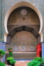 Fez, Morocco - man with red robe washes his hands in a water fountain in Fes el Bali. Monument with intricate mosaic tiles.