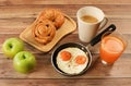 Ffried eggs , lattee coffee, orange juice ,croissant and danish pastry and two apples on wooden table Royalty Free Stock Photo