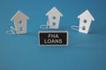 FHA mortgage loans symbol. Wooden houses sits next to a wooden black board with the word FHA loans. Beautiful blue background.