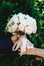 Fiance and the bride holds luxurious bridal bouquet of white peonies and roses in coniferous bushes