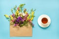 Field colorful flowers in craft envelope and cup of tea on blue