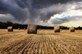 Field with hay bales under stormy sky and rays of light Royalty Free Stock Photo