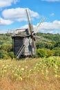 A field with ripening sunflowers against the background of an old wooden windmill and a rural antique summer landscape in a slight