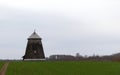 A field with a small tree and a windmill in the foreground Royalty Free Stock Photo