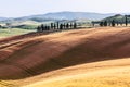 Fields in Tuscany and a lone farmhouse on a neighboring hill the horizon is covered with a light midday summer haze