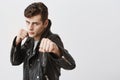 Fierce and confident european male model in black leather jacket with trendy haircut holding fists in front as if ready