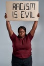 Fierce plus size young african american woman in casual clothes looking at camera, holding Racism is evil banner above