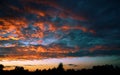 Fiery evening sunset, orange-blue color. On the horizon are silhouettes of houses and trees. Landscape, hectic clouds