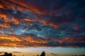 Fiery evening sunset, orange-blue color. On the horizon are silhouettes of houses and trees. Landscape, hectic clouds