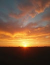 Fiery orange sky with clouds at sunset over a dark silhouette of a flat landscape. Sun setting on the horizon with bright rays Royalty Free Stock Photo