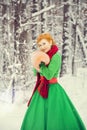 Fiery red-haired woman in a ball green dress with a red leather belt in the costume of dwarf assistant Santa Claus in the winter f