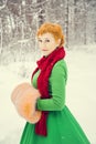 Fiery red-haired woman in a ball green dress with a red leather belt in the costume of dwarf assistant Santa Claus in the winter f