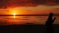 Brilliant sunset in the sea with the silhouette of a woman taking photos with her phone Royalty Free Stock Photo