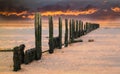 Fiery sunset sky over old water breaker, groyne on a wet sandy b