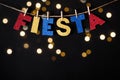 Fiesta word made of shiny paper and pins on black background and bokeh lights. Cinco de mayo concept