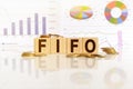 FIFO the word on wooden cubes, cubes stand on a reflective surface, in the background is a business diagram