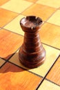 The figure of a black rook stands on a chess board.