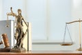 Figure of Lady Justice, gavel and books on table indoors, space for text. Symbol of fair treatment under law
