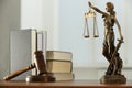 Figure of Lady Justice, gavel and books on wooden table indoors. Symbol of fair treatment under law