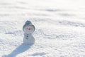 Figure of little cute snowman in a knitted hat and scarf on on snowy field in a sunny winter day.