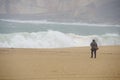 A figure of a woman walking on an empty beach in a storm