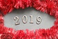 Figures 2019 on a wooden background, around the frame of Christmas tinsel red. Royalty Free Stock Photo