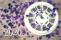 Figures 2020 on a wooden background next to purple pansy flowers and a white clock showing five minutes to midnight Royalty Free Stock Photo