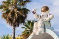 A figurine of an astronaut in a spacesuit holding a tube of food in his hand sits against the backdrop of palm trees and